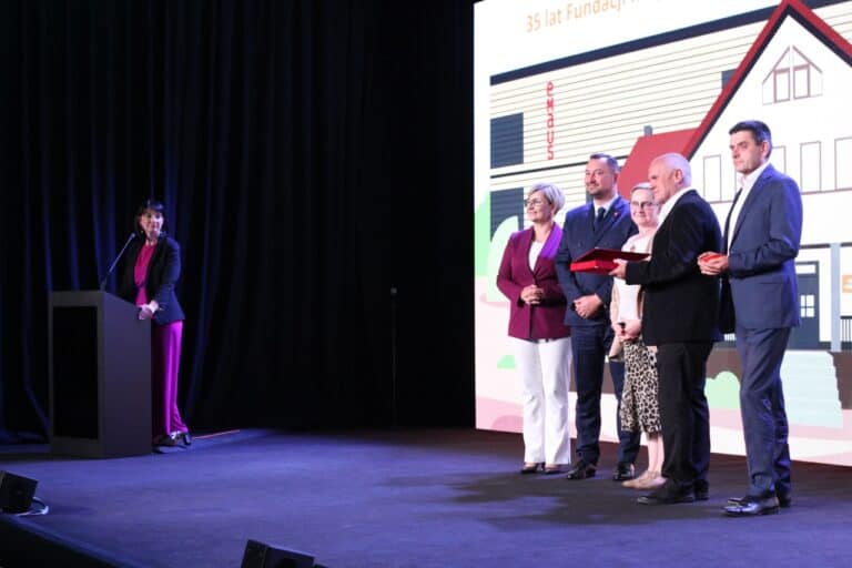 Pamiątkowa fotografia. Wicemarszałek Województwa Lubelskiego Marek Wojciechowski i osoby odbierające wyróżnienia i nagrody. Z lewej: przy mównicy, Iwona Kędziera