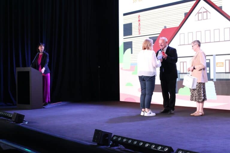 Od lewej, przy mównicy, prowadząca spotkanie Iwona Kędziera. W centrum kadru Zbigniew Drążkowski podczas wręczania wyróżnień