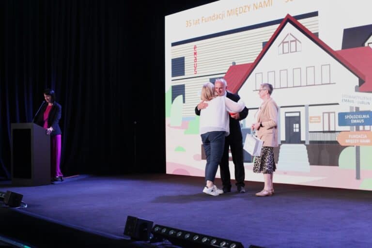 W centrum kadru Zbigniew Drążkowski podczas wręczania wyróżnień; po lewej stronie przy mównicy stoi prowadząca spotkanie Iwona Kędziera.