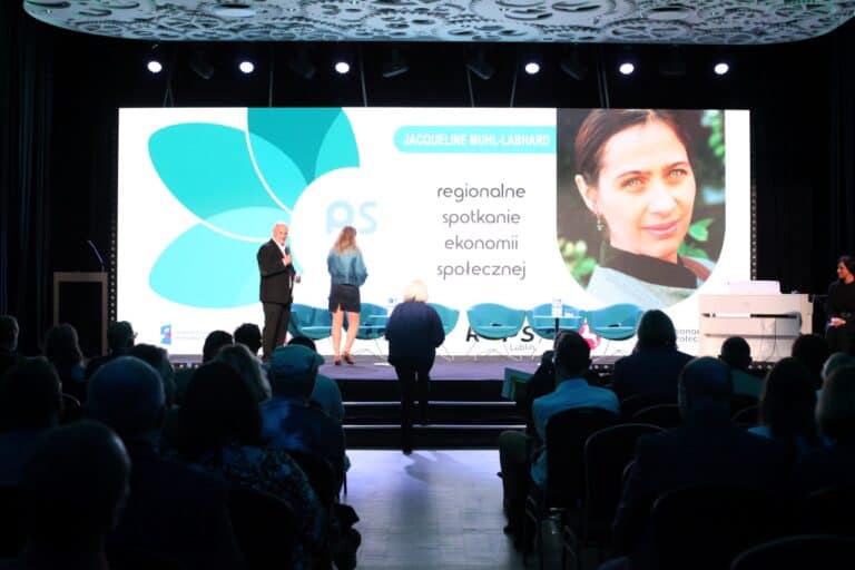 W centralnej części kadru Zbigniew Drążkowski zaprasza na scenę dwie kobiety. Jedną z nich jest Jacqueline Muhl-Labhard, współfundatorka Fundacji Między Nami. Jej imię, nazwisko i fotografia znajdują się na ekranie, stanowiącym tło sceny