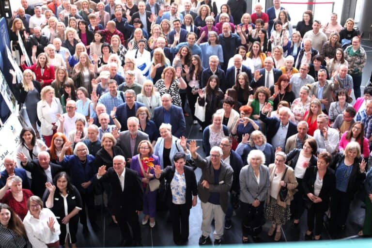Grupowe zdjęcie pamiątkowe. Fotografia zrobiona z perspektywy „lotu ptaka”. Pozujący goście uśmiechają się do obiektywu, machając radośnie.