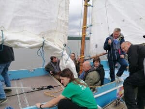 Na jachcie "Integracja" grupa osób obu płci szykuje się do wypłynięcia w rejs po widocznym w tle Zalewie Zemborzyckim. Niebo jest zachmurzone