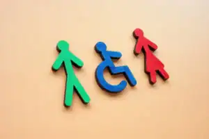 Trzy ikony przedstawiające mężczyznę (zielony), osobę na wózku inwalidzkim (niebieski) i kobietę (czerwony) na beżowym tle.