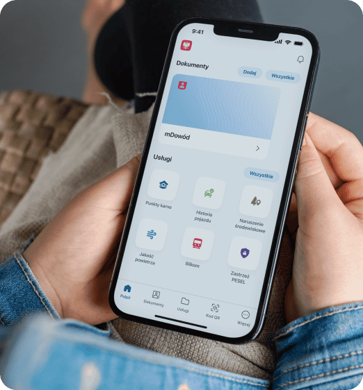 Osoba trzymająca smartfon wyświetlający na ekranie aplikację mObywatel z opcjami dokumentów i różnych usług.