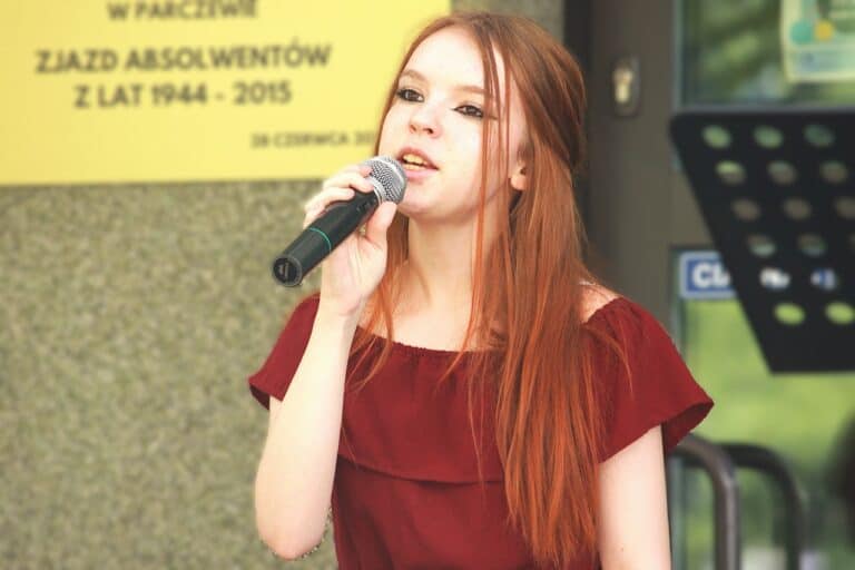 Portret uczestniczki przeglądu artystycznego. Dziewczyna trzyma mikrofon i śpiewa wpatrzona w dal