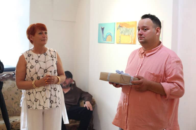 W prawej części kadru artysta trzymający w dłoniach prezent urodzinowy. Obok niego Maria Pietrusza-Budzyńska