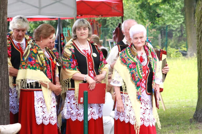 Trzy kobiety w lokalnych strojach. Mają na sobie czerwone spódnice, białe haftowane bluzki, czarne obszyte kamizelki i wielobarwne chusty z frędzlami, na których przeważają barwy: żółta, czerwona, niebieska, zielona