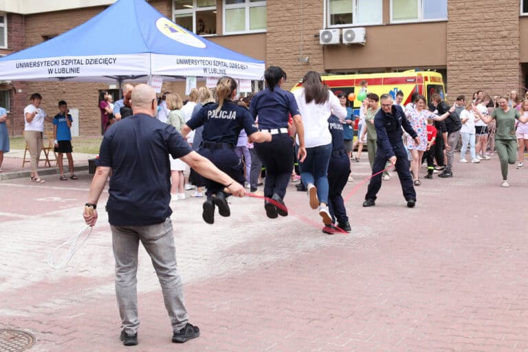 W kadrze dwóch mężczyzn trzymających długą skakankę, przez którą skaczą cztery kobiety. W tle uczestnicy akcji