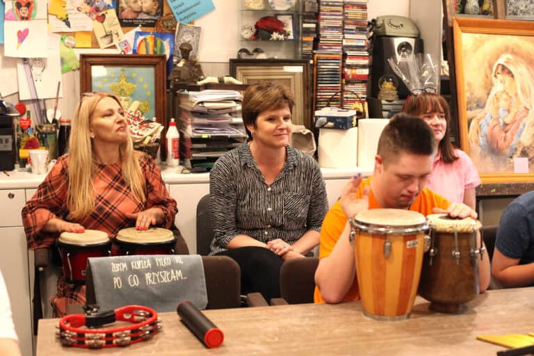 Na tle komody z akcesoriami plastycznymi od lewej: Anna Augustyniak, Zastępca Prezydenta ds. Społecznych (gra na bębnach), Joanna Olszewska, Dyrektor Wydziału ds. Osób Niepełnosprawnych. Po prawej chłopiec uderzający w bębny