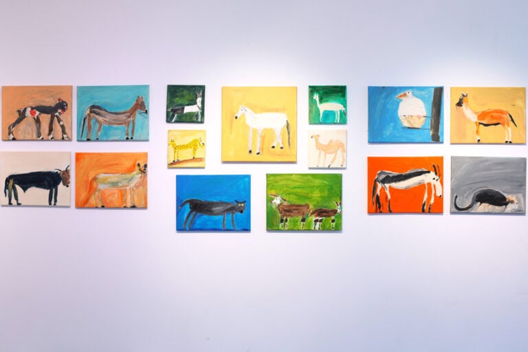 Ściana w galerii z piętnastoma obrazami bez ram, różnej wielkości, przedstawiającymi zwierzęta. Otoczenie obrazów jasne