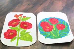 Rysunki podopiecznej warsztatów. Na dwóch białych kartonach rysunki czerwonych maków i zielonych liści. Na jednym z nich maki narysowano na tle niebieskiego okręgu