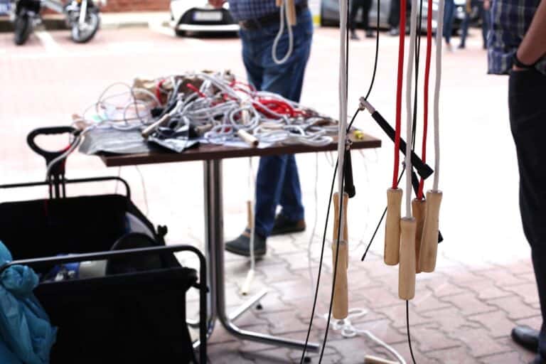 Zbliżenie na rączki skakanek. W tle stolik, na którym znajduje się kłębowisko odłożonych kolorowych skakanek