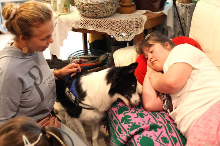 Od lewej: Violetta Rycaj-Lewandowska, pies terapeuta (Megi), leżąca na kanapie dziewczynka wpatrzona w psa