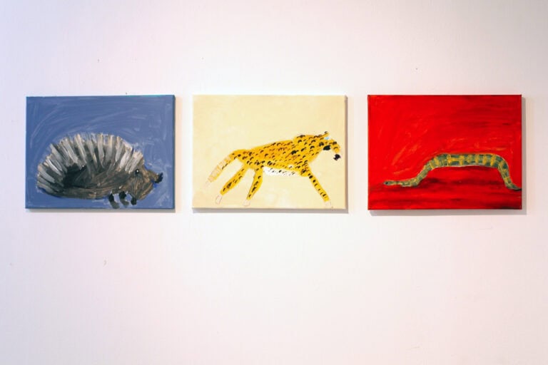 Trzy obrazy wiszące w jednym rzędzie. Wszystkie są kolorowe i przedstawiają zwierzęta. Wiszą na ścianie w jasnych barwach