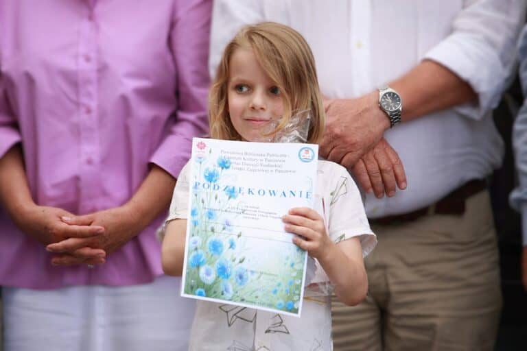 W centralnej części kadru chłopiec pozujący z otrzymanym Podziękowaniem (w formie dyplomu)