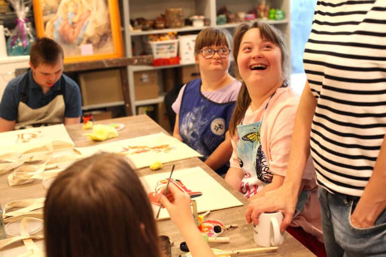 Dwie dziewczynki przy swoich pracach. Jedna z nich patrzy na kogoś, kto znajduje się poza kadrem, śmieje się radośnie