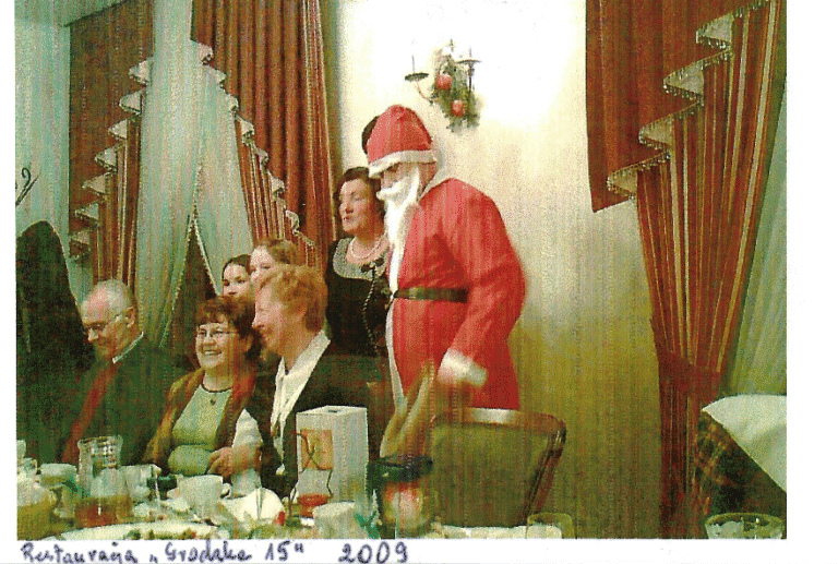2009 r. Spotkanie opłatkowe w Restauracji "Grodzka 15"; przy stole siedzą trzy kobiety, za ich plecami stoją cztery osoby, z których jedna ma na sobie przebranie Świętego Mikołaja