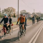 Na pierwszym planie: asfaltową szosą jadą dwa tandemy, w niewielkim oddaleniu za nimi widać jeszcze trzy rowery oraz samochody osobowe