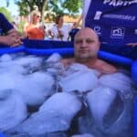 Mężczyzna zanurzony w ciemnoniebieskim dmuchanym basenie wypełnionym wodą i kawałkami lodu. Ponad powierzchnią widać tylko jego głowę, szyję i górną część ramion