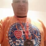 Łukasz Walczyński ubrany w pomarańczową koszulkę z pamiątkowym nadrukiem z biegu Wielkiej Orkiestry Świątecznej Pomocy "Policz się z cukrzycą" mającej na celu zbieranie funduszy na zakup pomp insulinowych dla kobiet w ciąży z cukrzycą. W 2021 roku bieg odbył się w nietypowej, hybrydowej formule, łączącej bieg stacjonarny z wirtualnym, ze względu na pandemię. Mężczyzna ma na szyi pamiątkowy medal