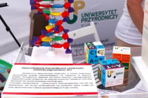 Od lewej: tabliczka opisująca Zwyrodnienie barwnikowe siatkówki, po prawej kostki 2x2 typu Rubika z napisami Lubelska Unia Cyfrowa i oznaczeniami w postaci liter. W tle kolorowy model dydaktyczny wykorzystywany do nauki biologii i napis Uniwersytet Przyrodniczy