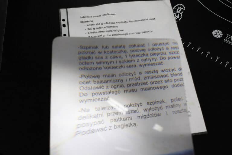 Fragment przepisu na sałatkę, na którym leży arkusz powiększający. Arkusz położony jest w około jednej trzeciej przepisu, pokazując różnicę w wielkości czcionki