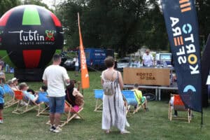 Od lewej duży reklamowy balon Lublin Miasto Inspiracji. Obok stoisko KartoSfery, przed którym na krzesełkach piknikowych siedzi grupa osób