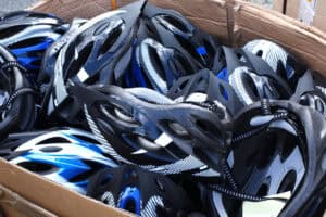 Rzut od góry na tekturowe pudełko z kaskami rowerowymi. Kaski mają barwy czarne, niebieskie i białe