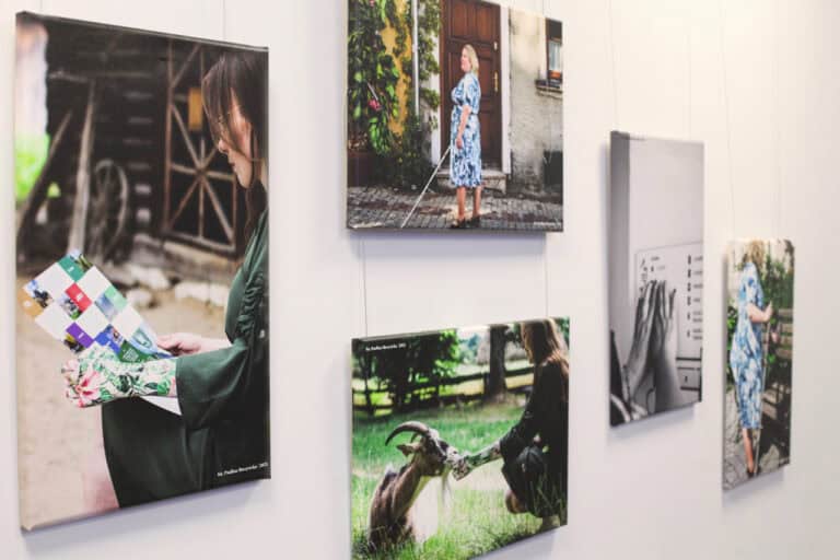 Na jasnej ścianie pięć fotografii rozmieszczonych asymetrycznie. Cztery z nich przedstawiają kobiety w rożnych pozach i miejscach. Piąta fotografia jest czarno - biała i jest to zbliżenie na dłonie