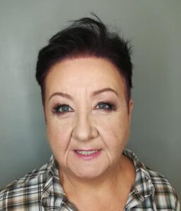 Elżbieta Sagan. Prosto w obiektyw patrzy uśmiechnięta, krótkowłosa brunetka w średnim wieku ubrana w koszulę w kratkę