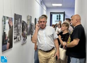 Mężczyzna przechodzi przez wystawę sztuki na korytarzu, a kilka osób ogląda zdjęcia na ścianie.