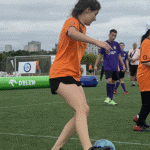 Zielona murawa boiska. Dziewczynka w pomarańczowej koszulce przy piłce