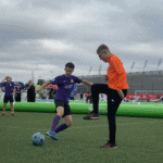 Zielona murawa boiska. Dwóch zawodników przy piłce, w tle stadion Arena Lublin