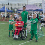 Przedstawiciele jednej z drużyn, w centrum chłopak w czerwonym stroju sportowym na wózku, obok niego trzech zawodników w zielonych strojach