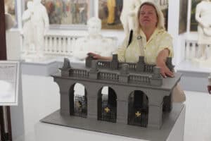 Miniatura Pomnika - Grób Nieznanego Żołnierza w Warszawie. Tuż za miniaturą stoi kobieta, której dłonie spoczywają na tym eksponacie. Kobieta ma zamknięte oczy. W tle wnętrze sali wystawienniczej