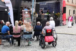 Przed sceną publiczność siedząca na krzesłach. Na pierwszym planie mężczyzna siedzący na wózku