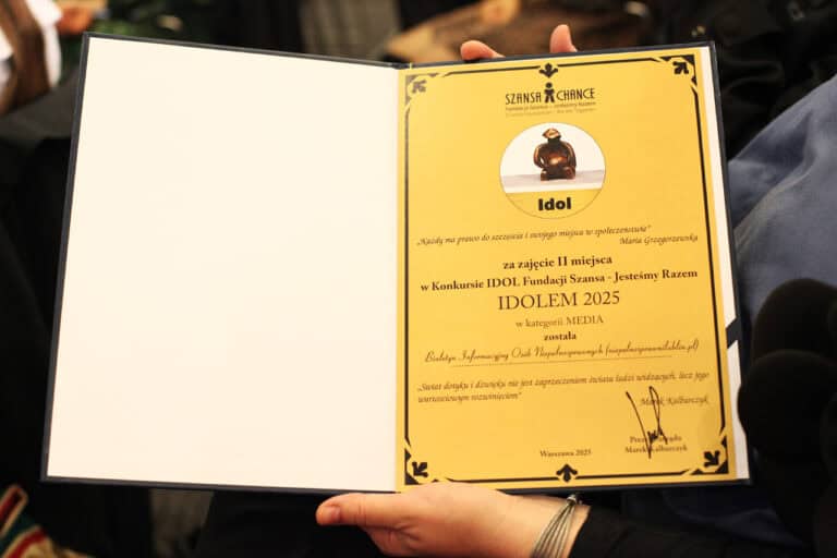 Zbliżenie na otwarty dyplom trzymany przez osobę. Prawa strona dokumentu jest w kolorze ciemnożółtym i zawiera tekst: "SZANSA CHANGE Fundacja Szansa" oraz tytuł: "Idol za zajęcie II miejsca w Konkursie IDOL Fundacji Szansa - Jesteśmy Razem w kategorii MEDIA" został/a Biuletyn Informacyjny Osób Niepełnosprawnych (niepelnosprawnilublin.pl). Widoczny jest podpis Marka Kalbarczyka i data: Warszawa 2025