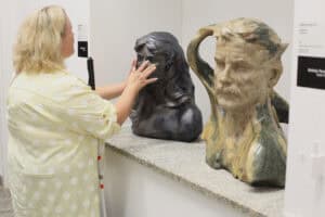 We wnęce w ścianie dwie rzeźby w kolorze czarnym i brąz. Od lewej kobieta z białą laską dotyka dłońmi ciemnej rzeźby