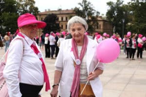 Plac Litewski w Lublinie. Dwie kobiety pozują do fotografii. Kobiety są ubrane na biało i mają na sobie dodatki w kolorze różowym. Kobieta z prawej trzyma różowy balon. W tle zgromadzeni ludzie