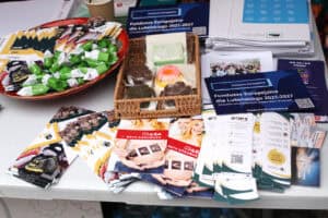 Rzut z góry na ekspozycję ulotek, broszur i folderów mówiących o funduszach europejskich i skutkach nałogów. Od lewej na tacy leżą cukierki typu krówka