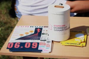 Na stoliku od lewej: plakaty i ulotki Sun Run, a także biała puszka na datki z napisem: "Hospicjum Dobrego Samarytanina"