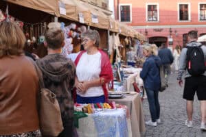 Rzut na stoiska wystawiennicze w perspektywie zbieżnej. Przed stoiskami zgromadzeni oglądający. W tle ściana kamienicy