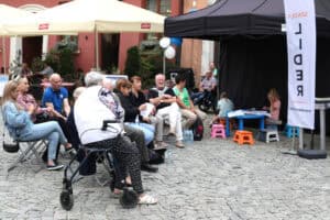 Rzut na publiczność siedzącą na krzesłach przed stoiskiem szkoły Lider. Na pierwszym planie od lewej kobieta siedząca na chodziku