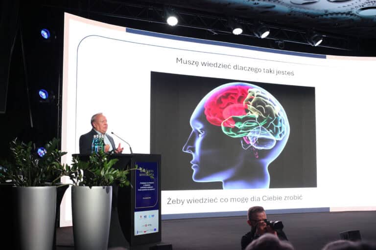 Widok na scenę. Od lewej, za mównicą mężczyzna (dr Ireneusz Siudem) przy mikrofonie. Reszta kadru, to widok na ekran multimedialny z napisem: „Muszę wiedzieć dlaczego taki jesteś, żeby wiedzieć co mogę dla ciebie zrobić” Na ekranie przedstawiono grafikę głowy z wyświetlonym na niej schematem ludzkiego mózgu