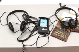 Na białym blacie leży urządzenie: audioprzewodnik i dwie pary słuchawek. Pod jedną z tych par, leżą dwa foldery informacyjne z napisem: „Muzeum Zamoyskich w Kozłówce”