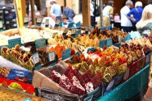 Wystawa stoiska. W pudełkach leżą poukładane kolorowe rachatłukum - wyrób cukierniczy kuchni tureckiej. Przy niektórych etykiety informujące o zawartości galaretowatych roladek, np. Nugat, orzechy, pistacje, ciasto filo