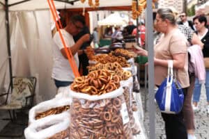 Rzut z boku na stoisko z preclami. Zbliżenie na plastikowe, przezroczyste worki wypełnione preclami. W tle inne stoiska i zgromadzeni kupujący
