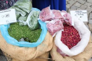 Dwa płócienne worki wypełnione od lewej: zieloną przyprawą czosnek niedźwiedzi, z prawej płatki róży. Na workach leżą małe woreczki z porcjowanymi już przyprawami