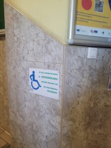 Informacja zamocowana na ścianie narożnej. Tekst brzmi: "W celu skorzystania ze schodołazu proszę zgłosić się do pracownika ochrony"