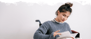 Kobieta na wózku inwalidzkim czyta książkę, ubrana w szary sweter